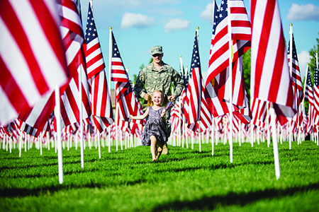 Military member walking with little girl through a field of American flags